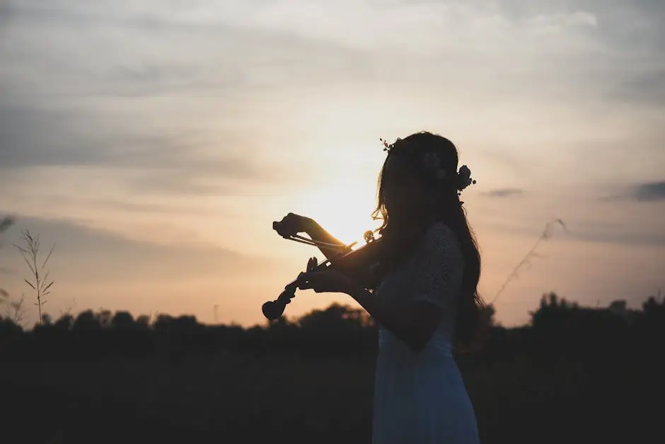 A woman plays violin in a serene field at sunset, creating a peaceful silhouette.